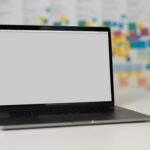 A laptop on a table with a blurred background of colorful sticky notes on a wall